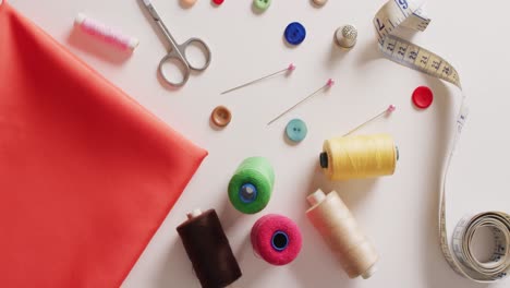 Video-of-fabric-with-tape-measure,-scissors,-buttons,-pins-and-cotton-reels-on-white-background