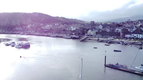 idyllic conwy castle and harbour fishing town coastal waterfront aerial reverse over boats below