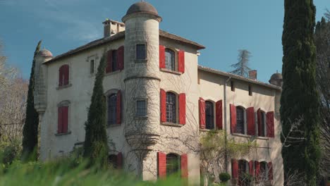 Ein-Wunderschönes-Südfranzösisches-Schloss-Mit-Roten-Fensterläden-Und-Türmen,-Vom-Boden-Aus-Betrachtet,-Während-Der-Wind-Das-Gras-Weht