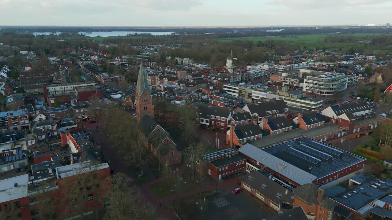 Drohnenaufnahme einer Kirche, umgeben von Wohnhäusern und Straßen in Haren, Niederlande, im Winter. Ruhige Stadtlandschaft mit bedecktem Himmel, von oben gefilmt