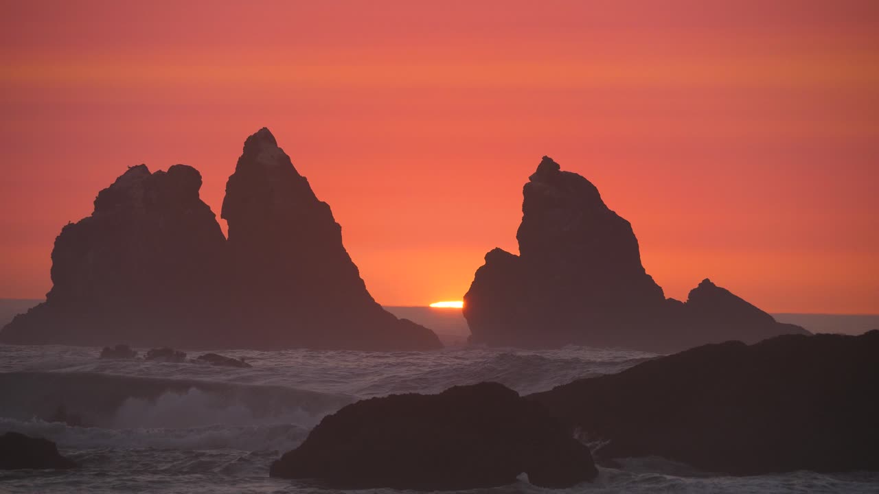 dos pilares atraviesan la neblina roja mientras el sol se desvanece en una playa de oregon