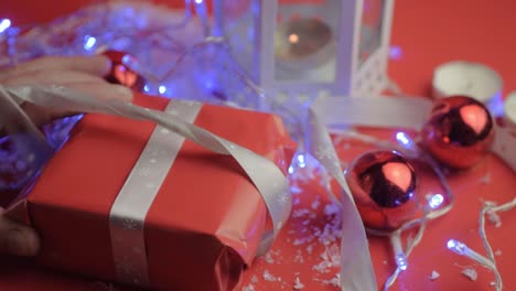 Untying-a-silver-bow-ribbon-on-Christmas-gift-with-red-paper-with-red-background-and-baubles