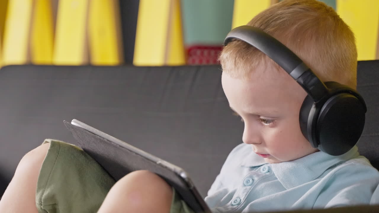 молодой мальчик смотрит планшет, нося наушники