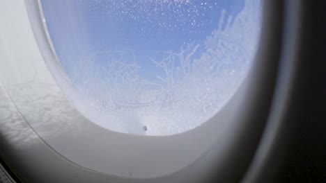 frost-covered window of airplane with clear blue sky outside, captured at high altitude