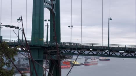 automóviles y autobuses que cruzan un puente colgante con camiones cisterna anclados en el fondo en un día nublado de invierno