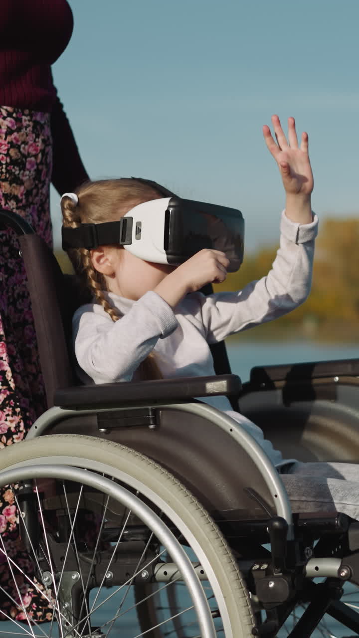 una joven madre está de pie junto a su hija con una lesión en la médula espinal cerca del lago. una niña en edad preescolar juega un juego usando gafas de realidad virtual en un fondo borroso