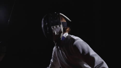 two women fencers compete in a dark indoor setting.