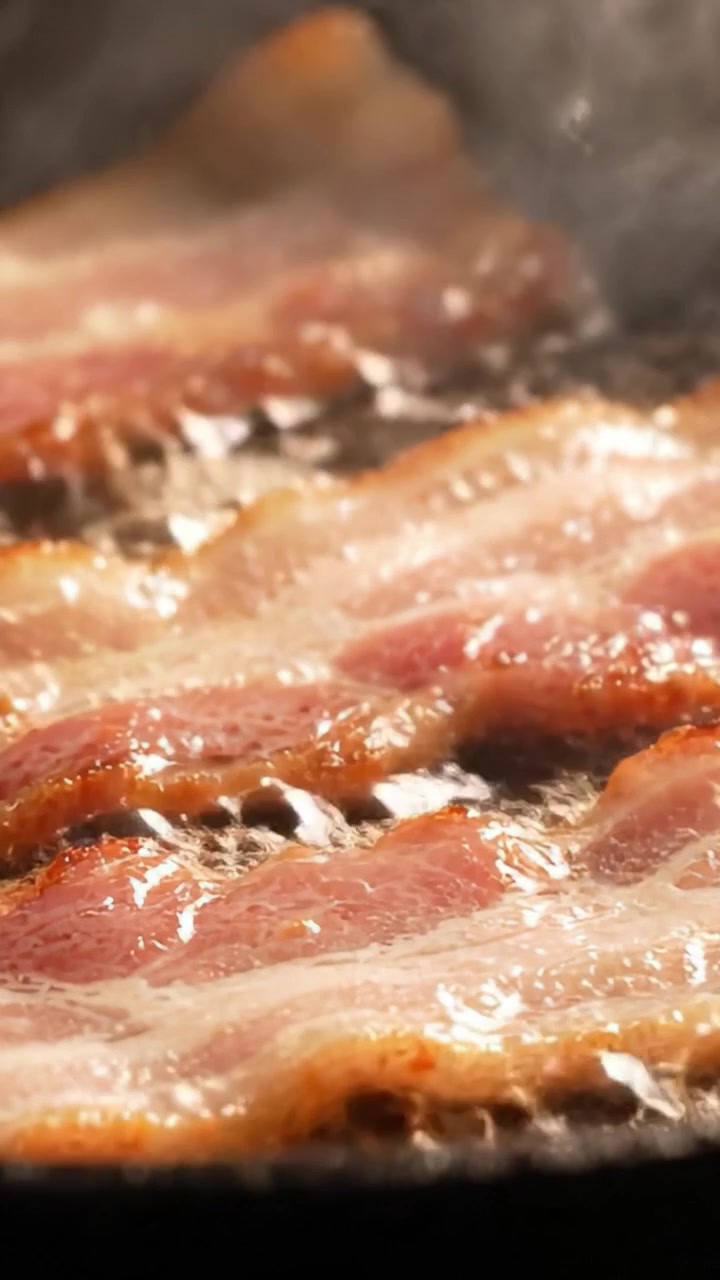 Processo di cottura del bacon sfrigolante: una vista ravvicinata di strisce di bacon che friggono nell'olio per delizie della colazione, emanando un aroma e un sapore da acquolina in bocca.