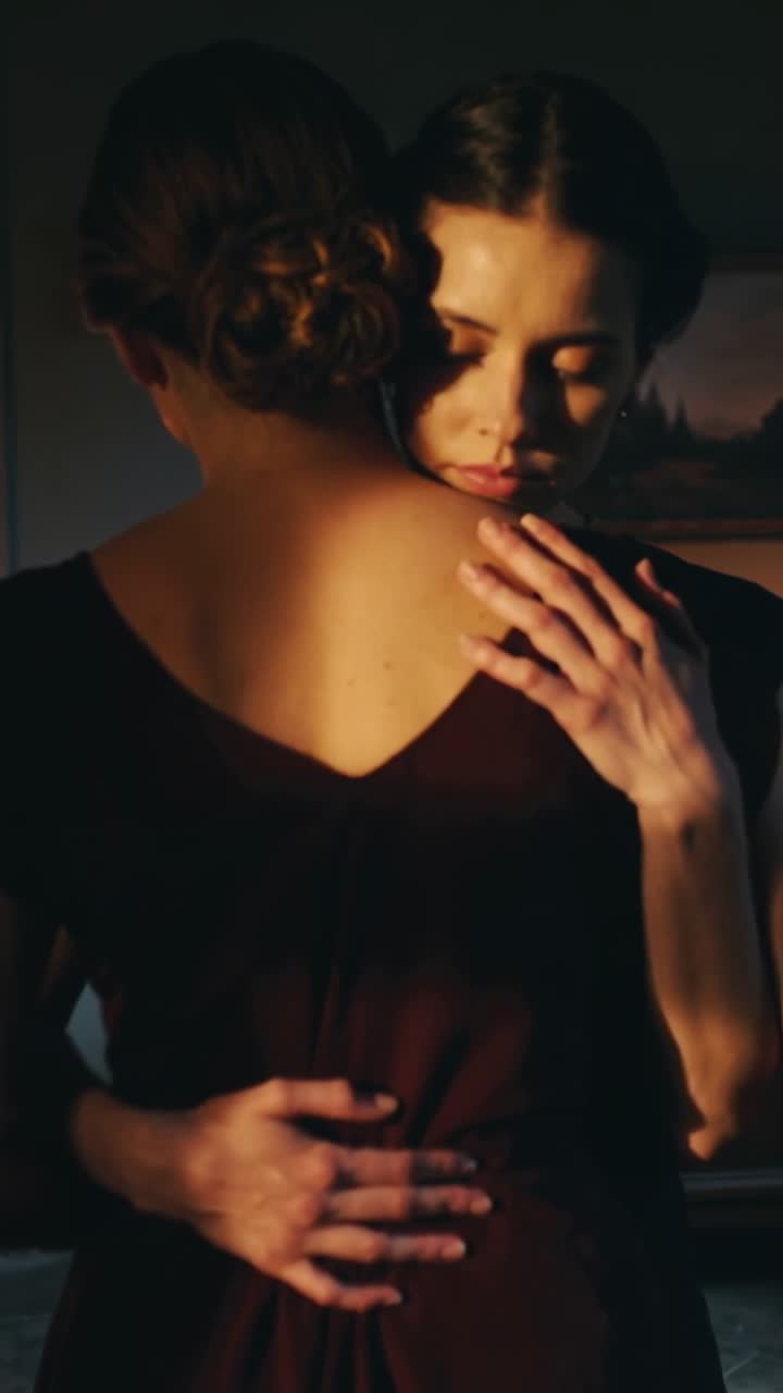 Vertical video: Coming woman hugging lover in burgundy dress at home by frame warm light comforting