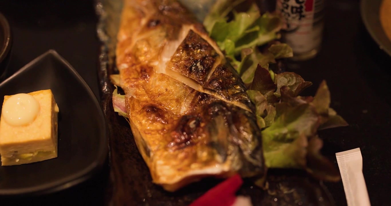 High angle close up of grilled saba mackerel served with side dishes in warm lighting.