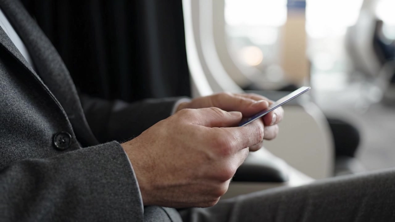 Uomo in abito che usa lo smartphone mentre è seduto in uno spazio moderno, impegnato in comunicazione o interazione con un'app, concentrato su un compito digitale in un ambiente confortevole.
