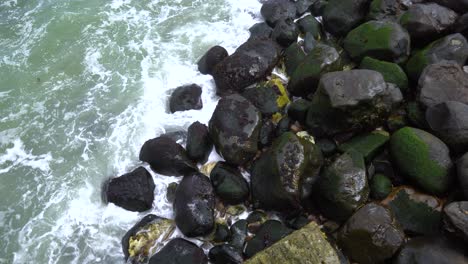 Olas-Rompiendo-Contra-Rocas-Cubiertas-De-Musgo-En-La-Orilla,-Vista-Desde-Arriba