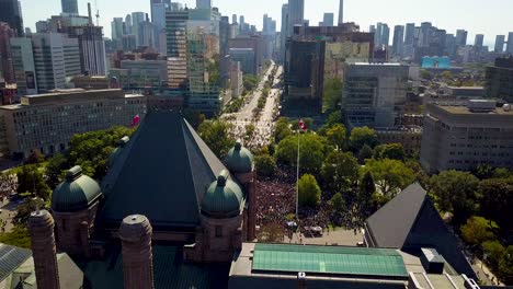 aerial view of downtown toronto and ontario legislature, wide daytime fixed shot in 4k. old building looms over crowd of people on front lawn as city skyscraper buildings tower in panorama background