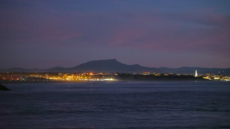cinematográfico impresionante dramático noche noche crepúsculo luces de la ciudad faro brillando biarritz hossegor francia playa montaña paisaje costero biarritz país vasco bahía de agua tranquila todavía trípode