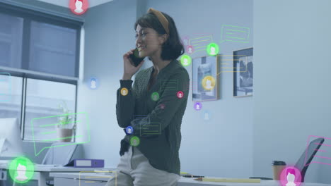 animation of social media icons over biracial businesswoman talking on smartphone at office