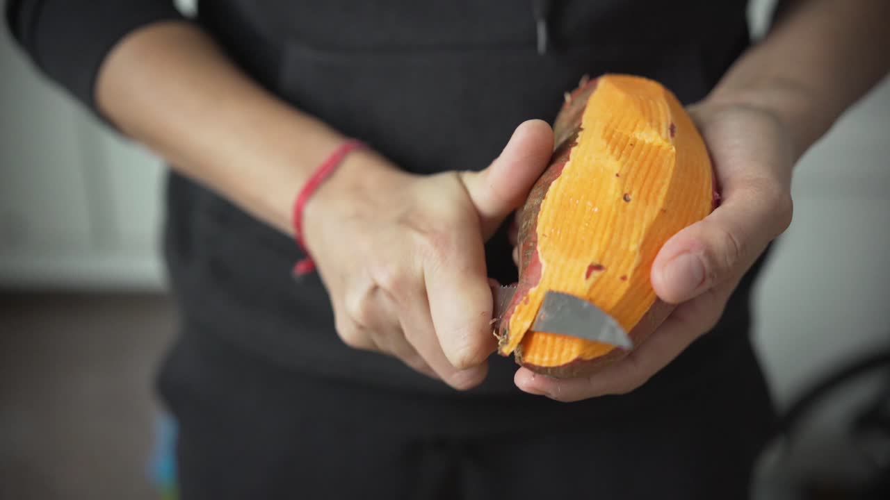 Close up of woman hands peeling a sweet potato with a knife, front view, cooking fresh organic vegetables