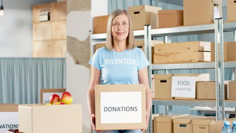 caucasian woman volunteer holding donation boxes and looking at camera in charity warehouse