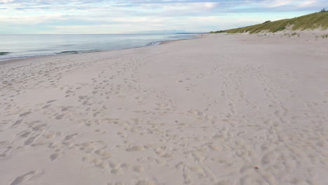 aerial: very slow flying above sandy beach with foot prints and seashore on the side