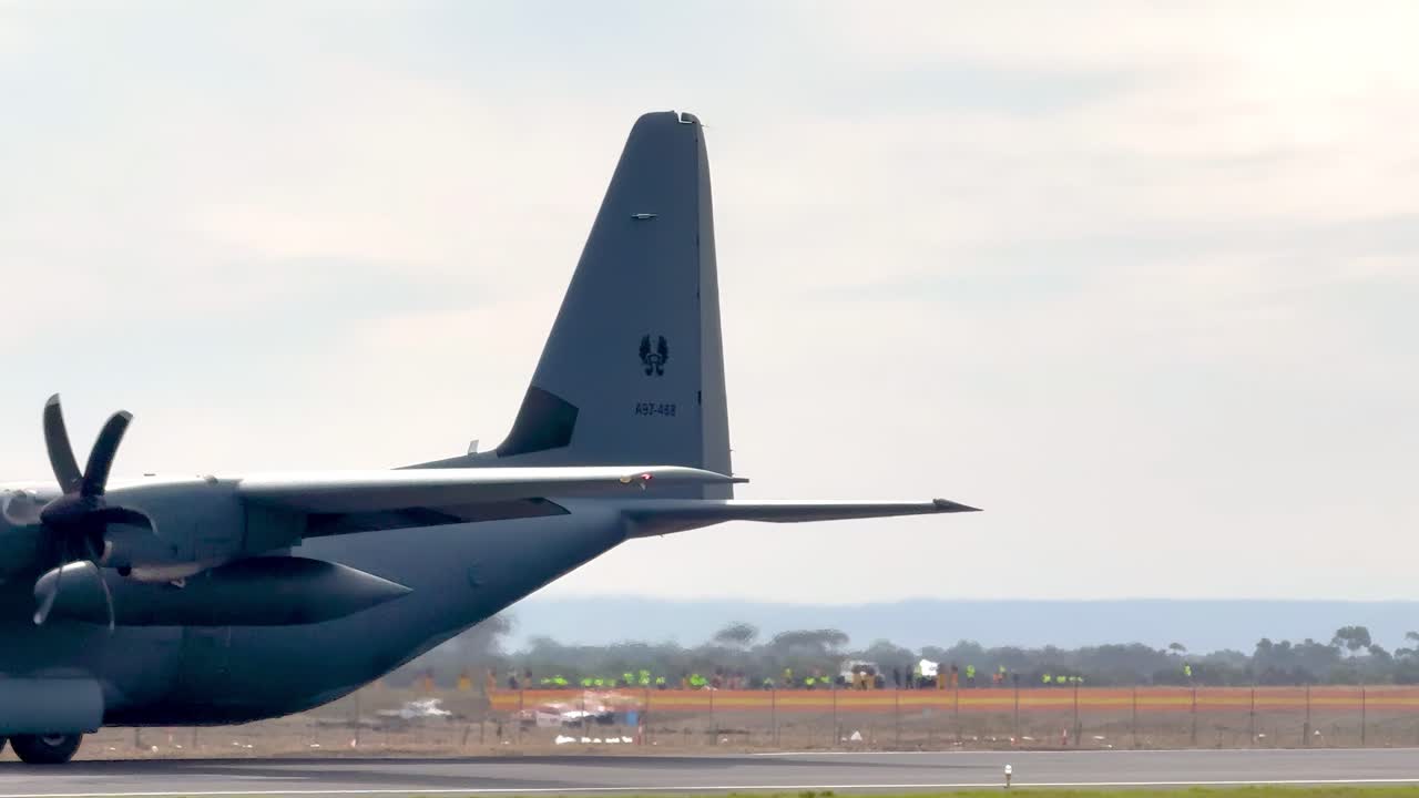 A close-up view of a C-130J aircraft taxiing on a runway with propellers spinning.
