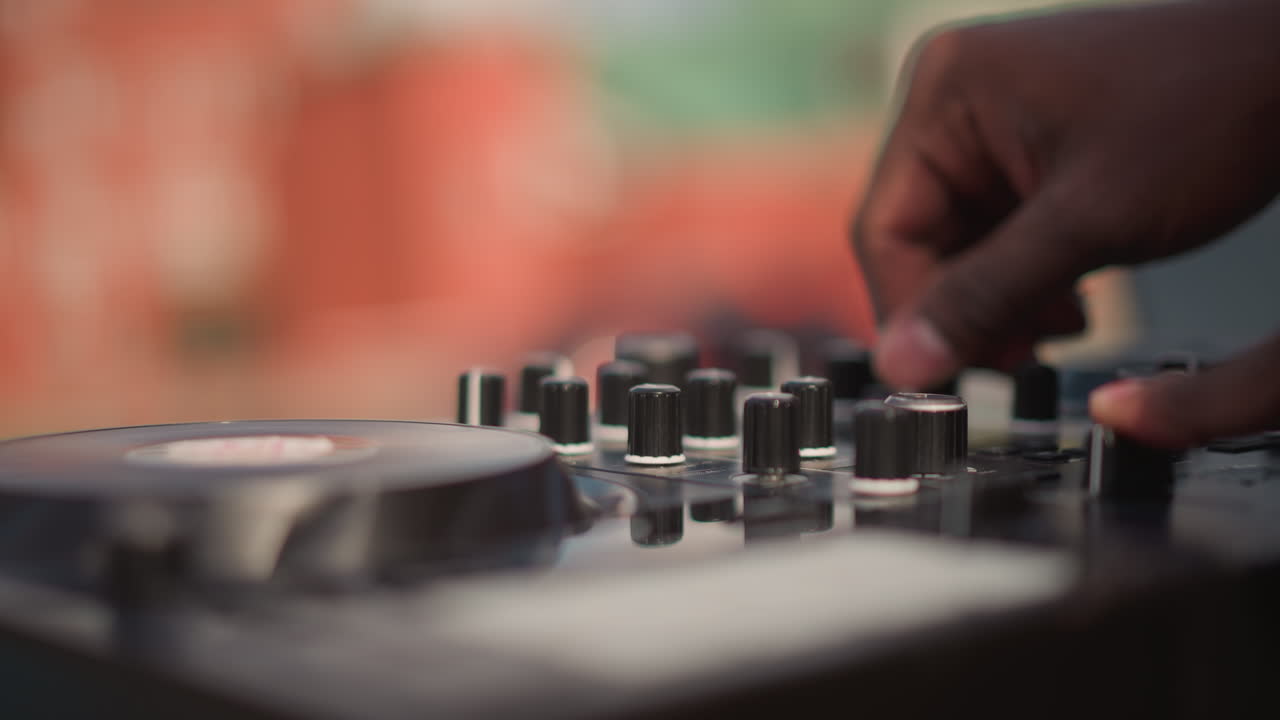 Mani di DJ nero sul mixer, DJ di strada su tetto che si sta riscaldando regolando l'equalizzatore e mettendo in coda i brani, artista di strada mobile che bilancia i livelli, tecnico del suono per eventi che controlla i medi, produttore che crea un groove morbido.