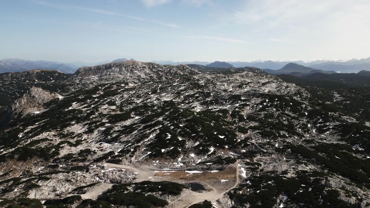 Vasta cordilheira com superfícies rochosas e manchas de neve estende-se pelo horizonte, revelando picos e vales em um cenário natural durante o dia.