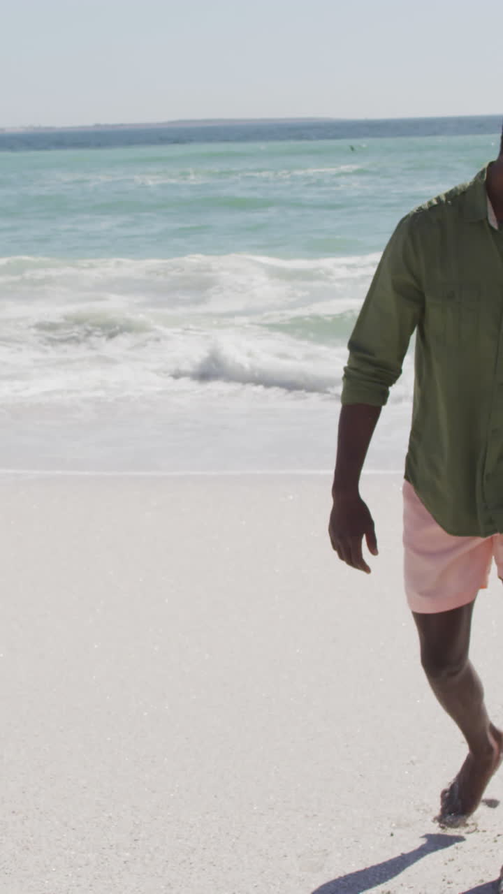 padre afroamericano sonriente con su hijo caminando por una playa soleada