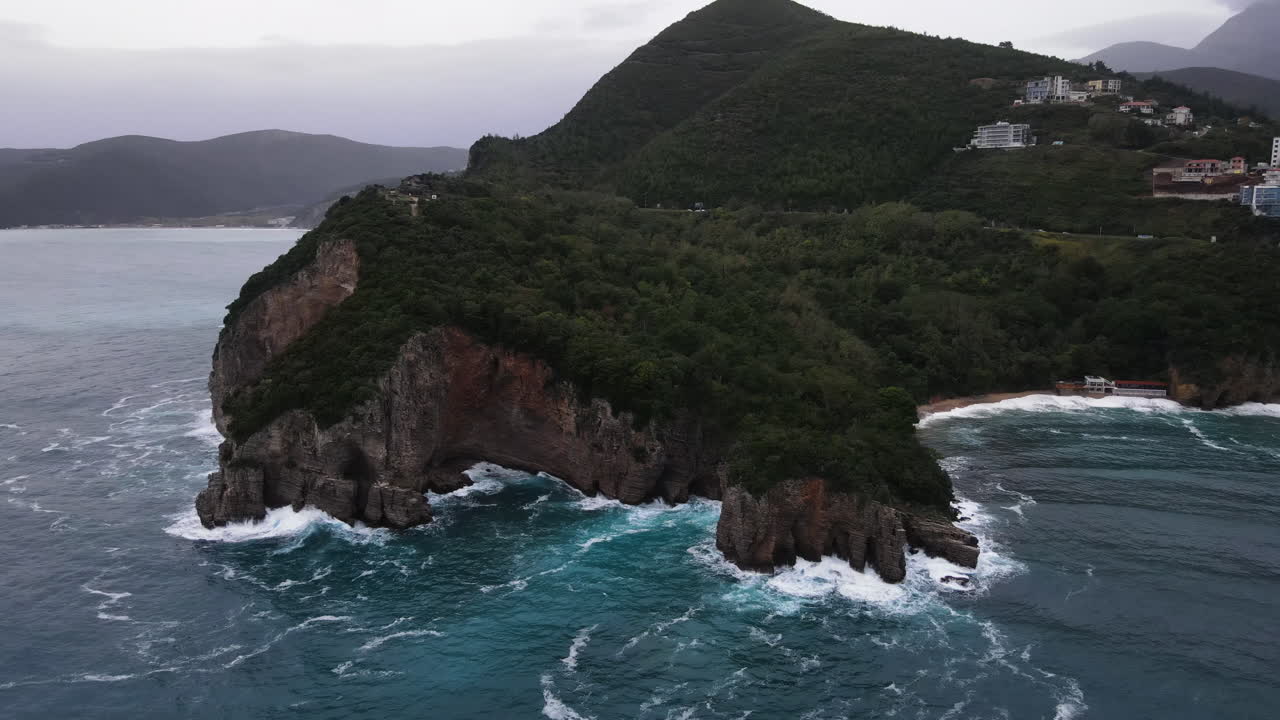 Aerial drone shot over the scenic cliffs and lush green vegetation over the mountainous terrain with Adriatic sea below in Montenegro on a cloudy day