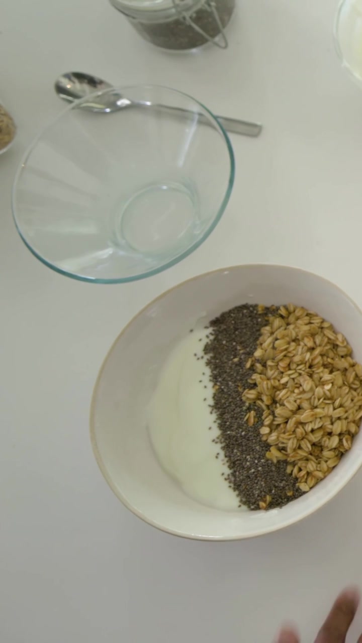 Video verticale: Donna in viola che prende e mette l'avena in una ciotola sul bancone di casa per mangiare, spazio per il testo