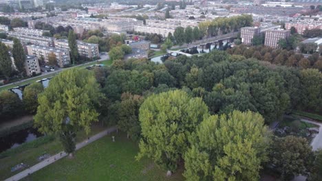 green treetops in the corner of a park with an inner canal surrounding it and people running on its paths in famous amsterdam, aerial view