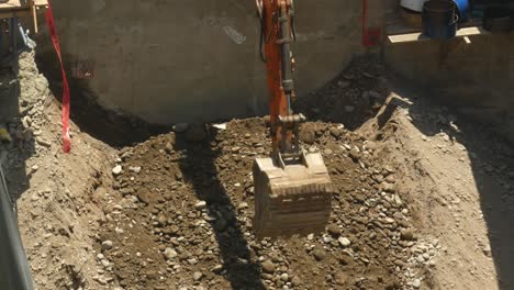 an excavator scooping up debris, rubble and rocks up from a mound in a construction site