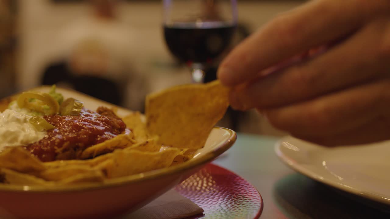 Mano che intinge una tortilla chip nella salsa con panna e avocado, illuminazione calda, atmosfera rilassata