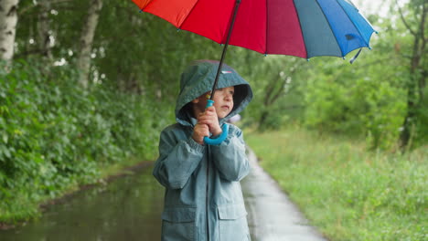 a young boy walks through a forest on a rainy day with a colorful umbrella