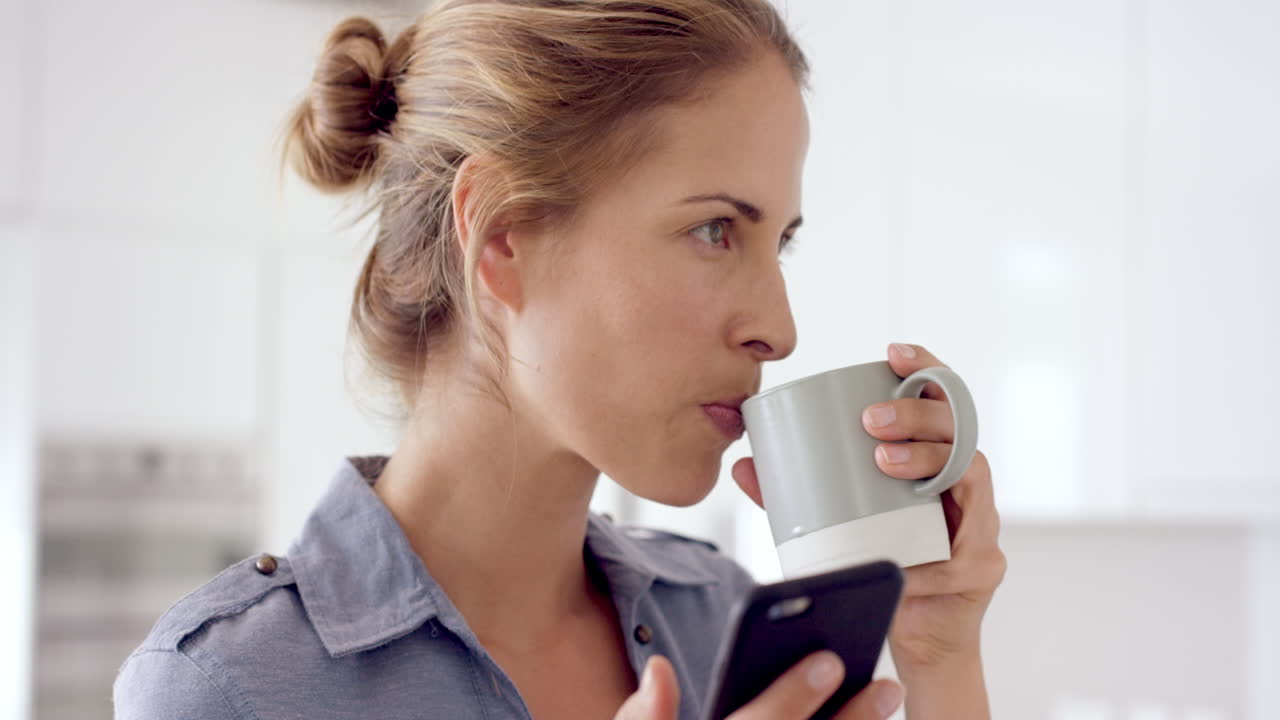 En kvinde bruger mobiltelefon derhjemme, drikker kaffe og nyder en afslappet livsstil.