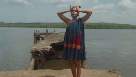 a young woman in a dress stands on the shore of the lake and enjoys nature