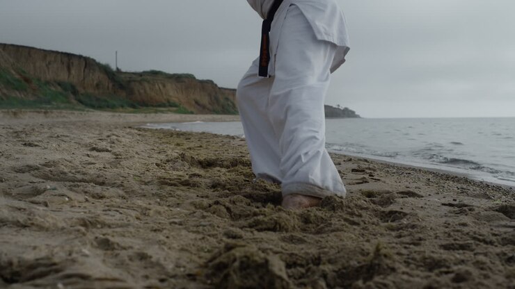 Piedi di un uomo che calpestano la sabbia della spiaggia praticando karate con tempo nuvoloso, in primo piano.