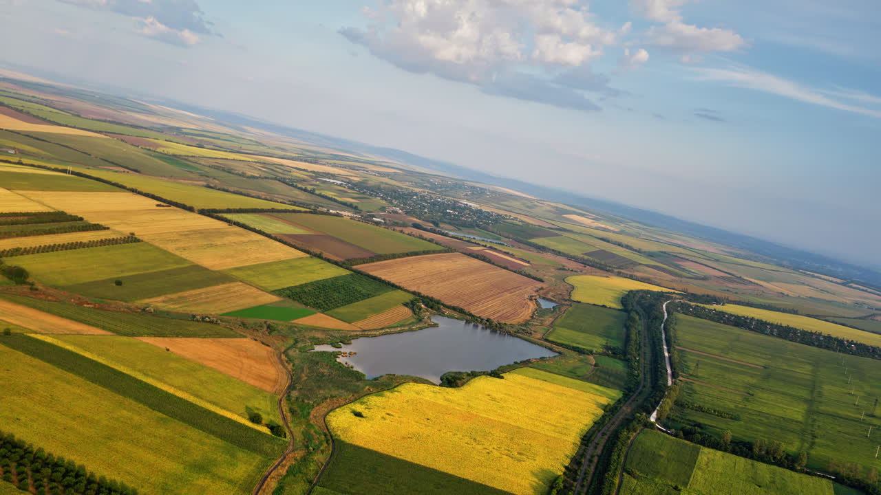 Aerial drone view of the vast Moldovan countryside with colorful patchwork fields stretching to the horizon under a partly cloudy sky