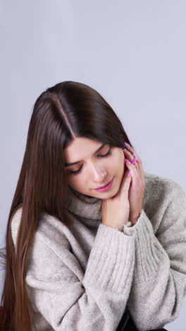 beautiful long-haired young lady sitting in armchair indoors. attractive woman bent her head looking down. white backdrop. vertical video