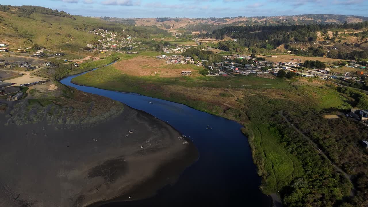 Movimento cinematográfico de drone com inclinação para cima e zoom, da lagoa costeira de zonas húmidas até a cidade rural de La Vega de Pupuya, no Chile.