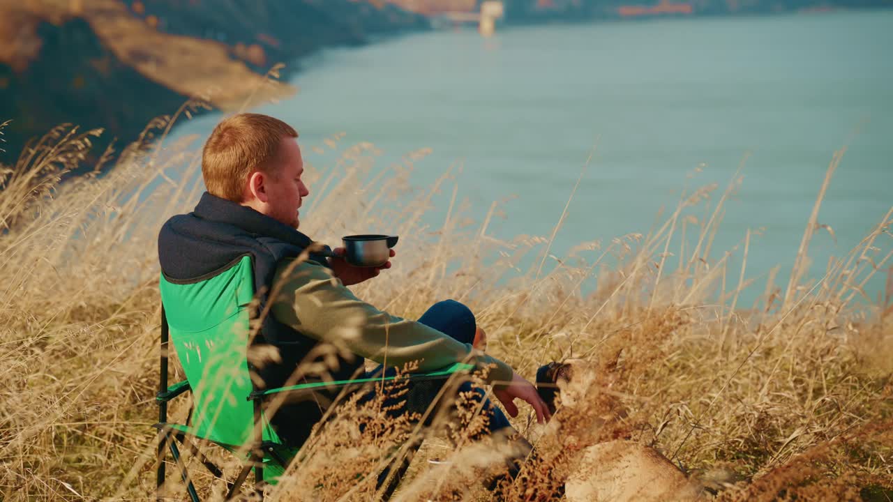 Un momento di serenità catturato nella natura: un uomo seduto in riva a un lago pittoresco si gode lo splendido paesaggio in compagnia del suo fedele cane, creando una perfetta rappresentazione di tranquillità e compagnia all'aria aperta.
