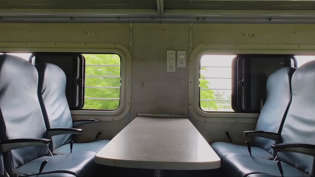 Lento zoom-in su sedili vuoti accanto al finestrino in un treno indiano in movimento, atmosfera tranquilla di viaggio e solitudine.