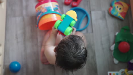 High-angle-shot-of-an-adorable-future-generation-one-year-old-asian-boy-playing-by-himself-with-a-colorful-toy-train-inside-a-beach-bucket-at-home