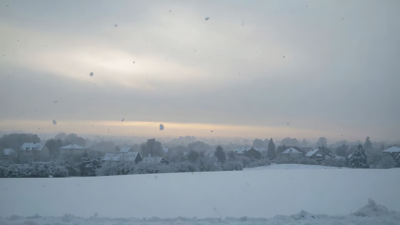 Brightening low horizon sunlight bathing snow-covered field and row of houses at rural outskirts