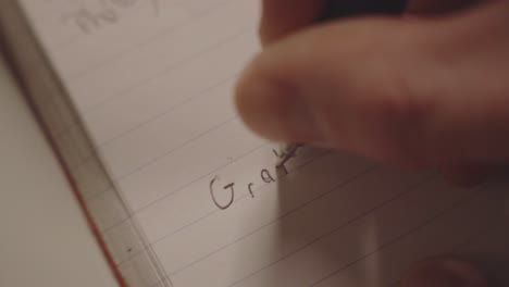 person's hand with a pen writing word grateful in a notebook