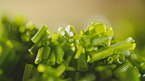 close macro shot of fresh chopped chives laying on a wooden cutting board, then water is sprayed on it