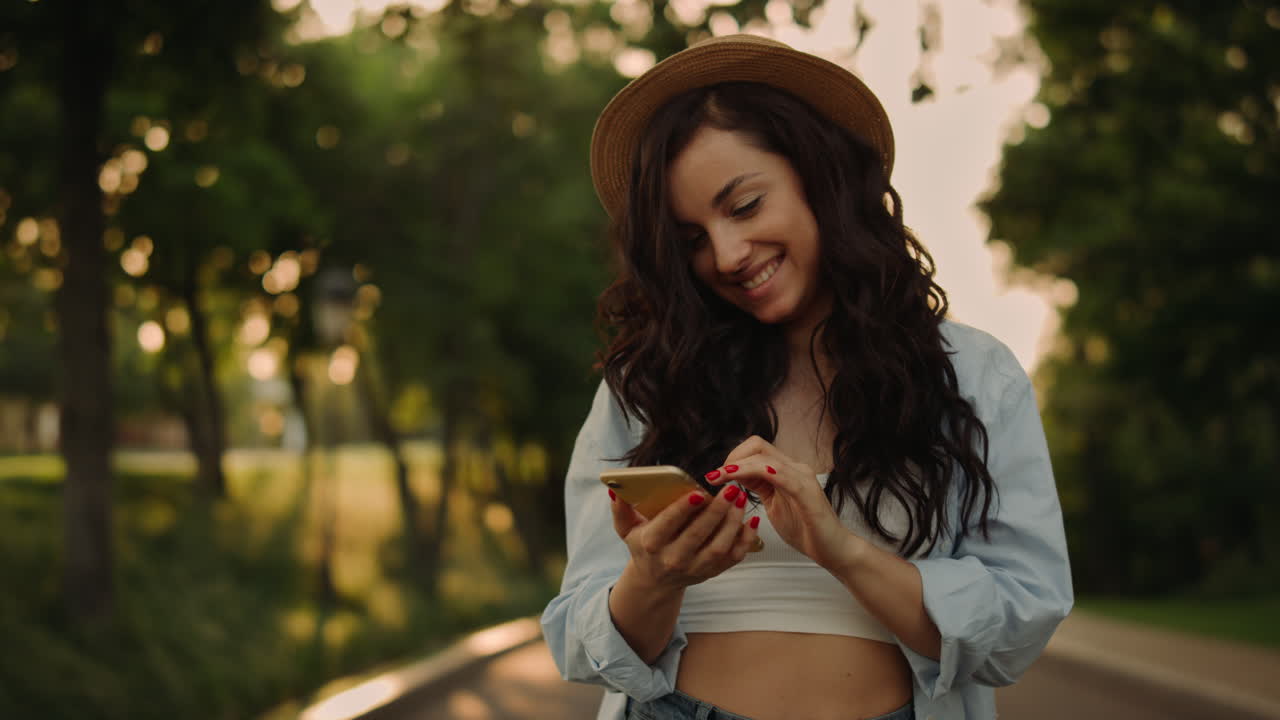 Mujer emocionada usando el teléfono móvil en el parque. Mujer positiva caminando con su smartphone.