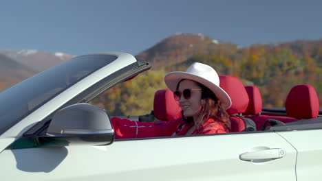 mujer conduciendo un coche descapotable a través de las pintorescas montañas de otoño