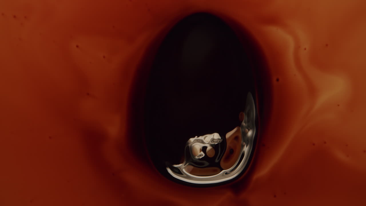 toma superior de una pequeña gota de aceite en un líquido ámbar oscuro que es arrastrado por un imán debajo