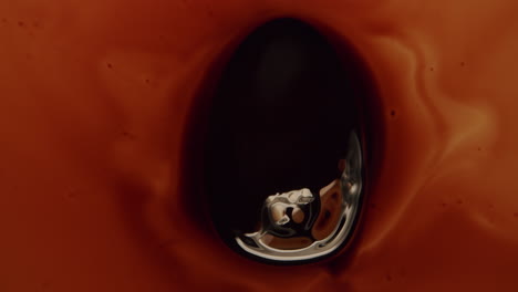 top shot of a small oil drop in a dark amber liquid getting pulled around by a magnet underneath