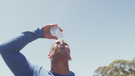 Fit-african-american-man-pouring-water-over-shaved-head,-cooling-off-after-exercising-in-the-sun