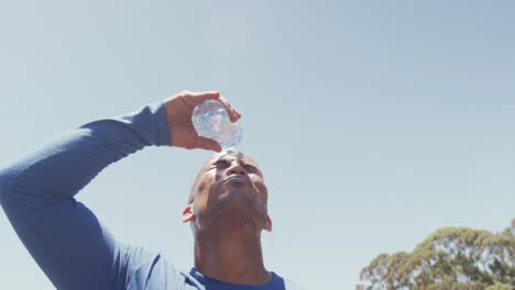 Hombre-Afroamericano-En-Forma-Vertiendo-Agua-Sobre-La-Cabeza-Afeitada,-Refrescándose-Después-De-Hacer-Ejercicio-Bajo-El-Sol